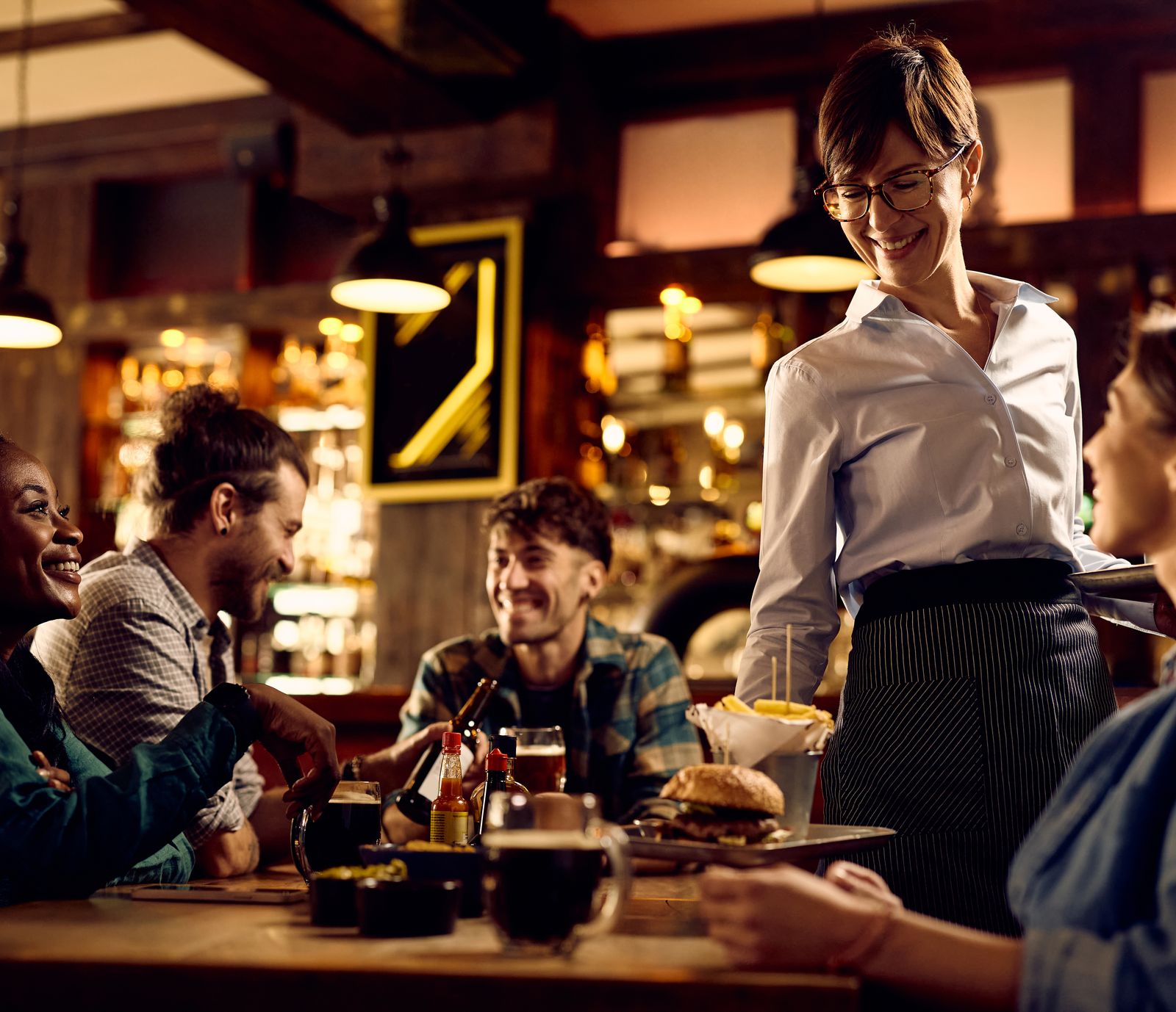 Server bringing food to friends laughing at a restaurant table